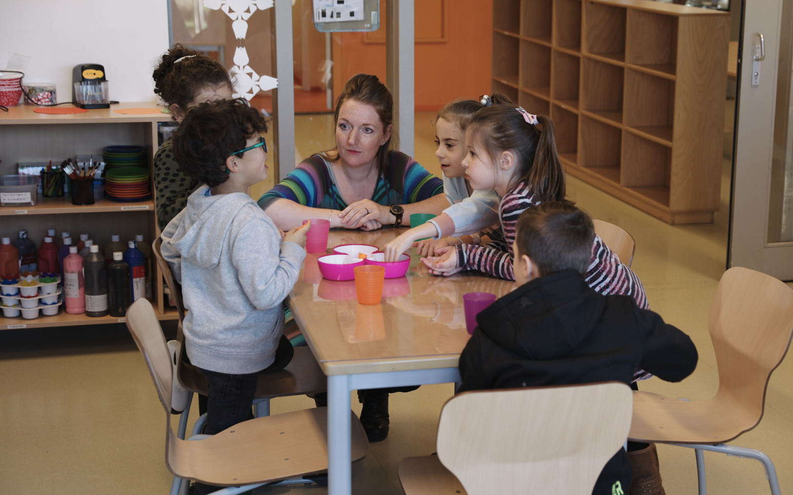 Vrouw gehurkt aan tafel met zes kinderen