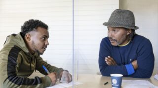 foto van twee mannen die praten met een spatscherm ertussen