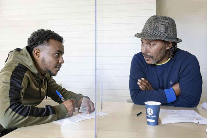 foto van twee mannen die praten met een spatscherm ertussen