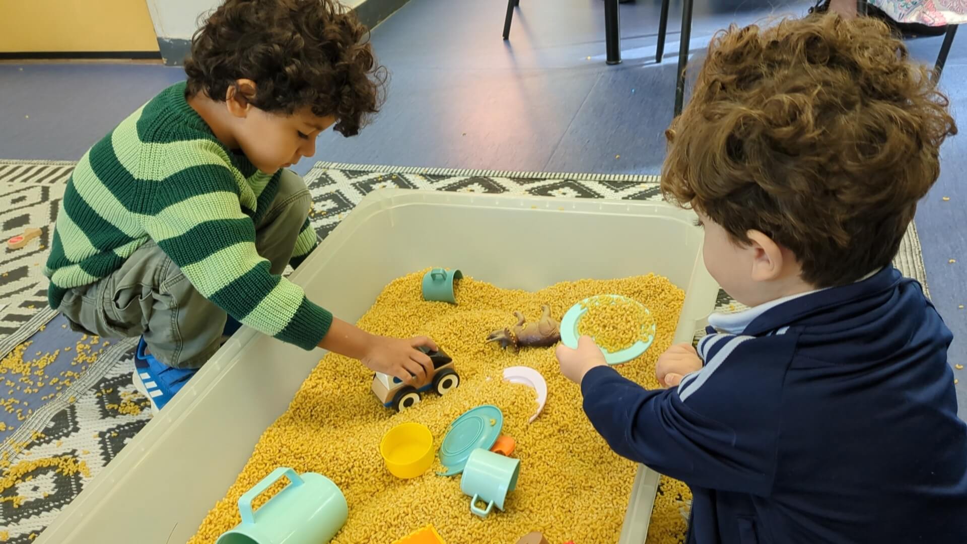 Twee kleine kinderen spelen in bak met macaroni