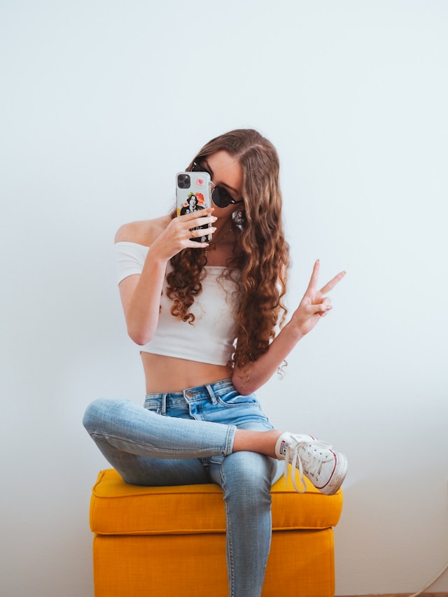 foto van een meisje dat op haar telefoon kijkt en een peace teken maakt