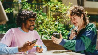 twee mensen aan een tafel. De ene laat diens telefoon zien aan de de andere persoon