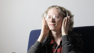 een vrouw in kleermakerszit op de bank met een koptelefoon op